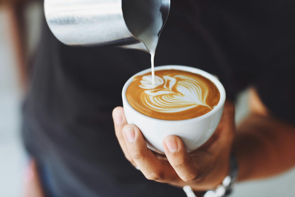 Someone holding a fresh cup of coffee and pouring in milk foam. 