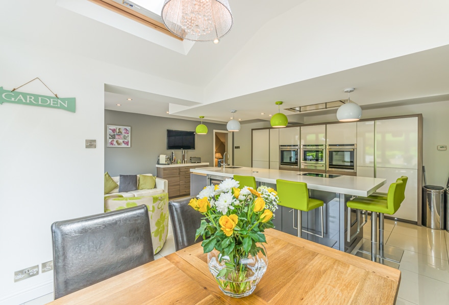 Dining room table with bright yellow and green flowers on showing an open plan kitchen design for Adamsons
