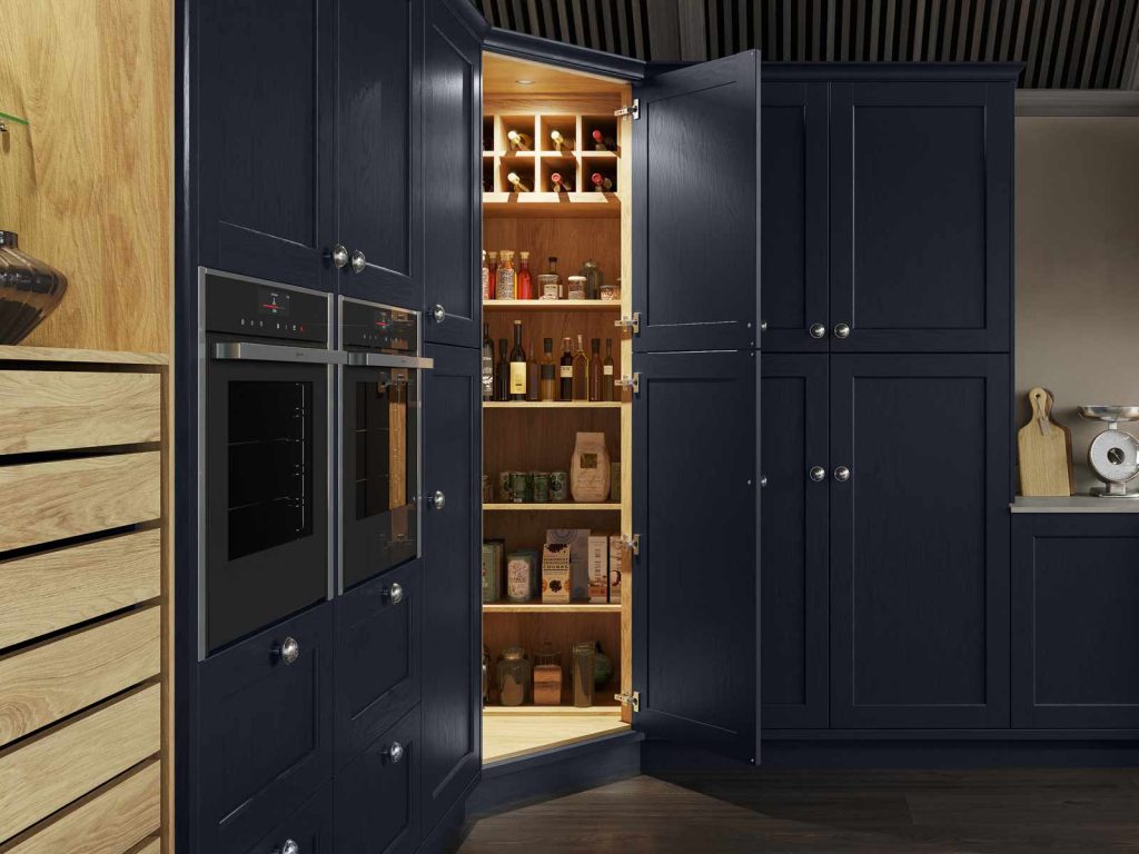 A navy blue corner pantry with warm lighting coming from an open cabinet door