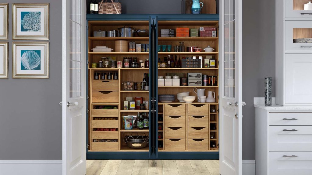 A built in pantry set behind two white doors with glass. The pantry has a deep navy frame with light oak drawers and shelves