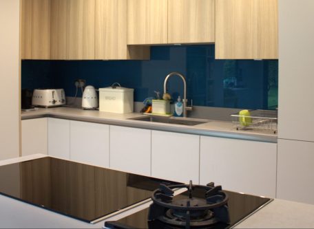 A modern kitchen with dark blue glass splashback, light oak cabinetry and modern, black appliances