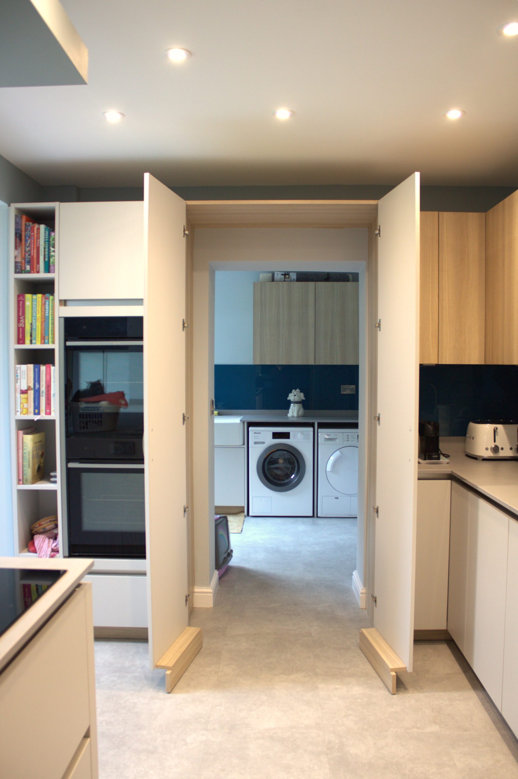 Open cabinet doors reveal a secret utility room with a modern washing machine and tumble dryer